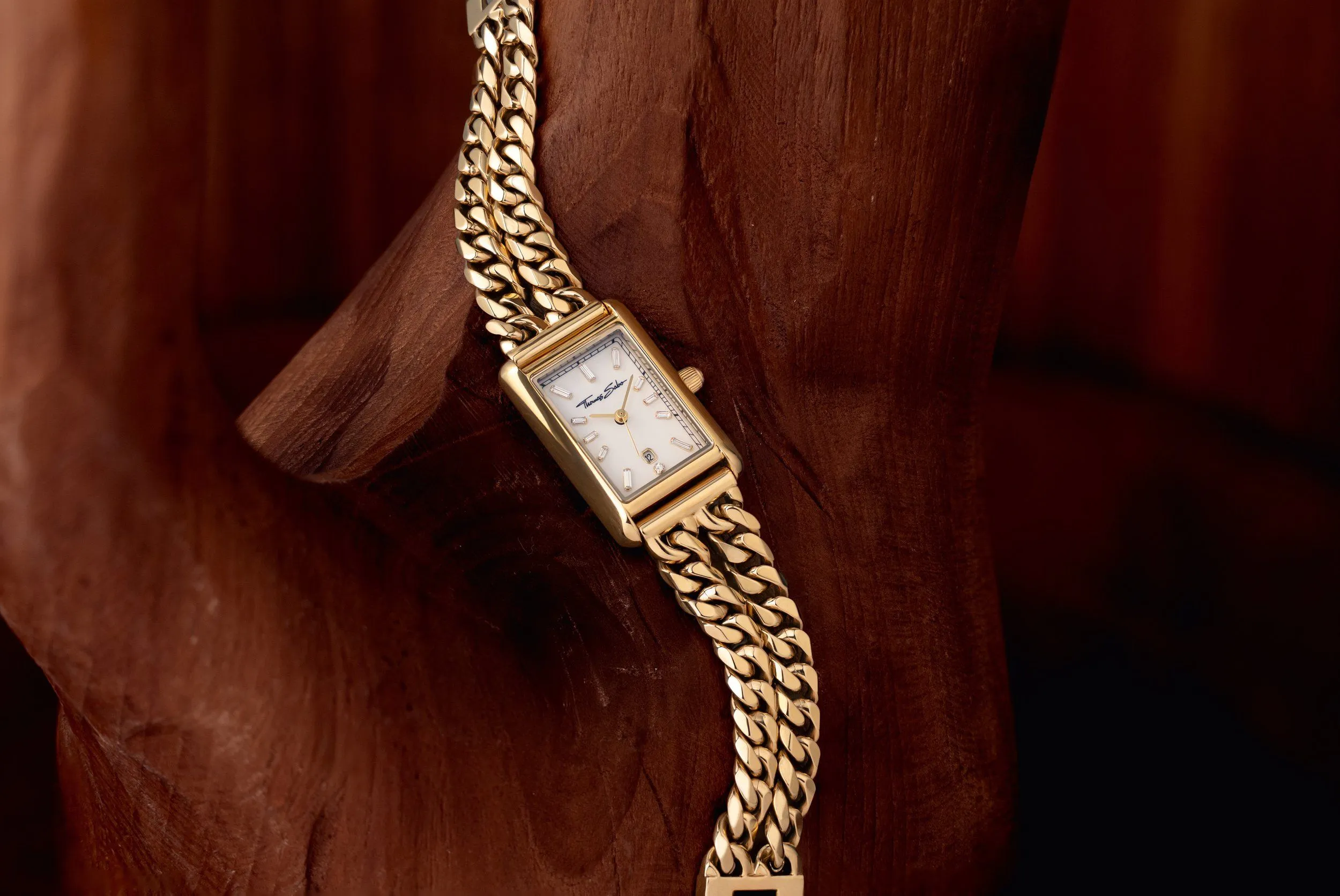 A gold wristwatch with a rectangular face and metal band, resting on a wooden surface.